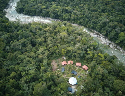 A series of structures with tile roofs next to a bending river that flows through an immense jungle