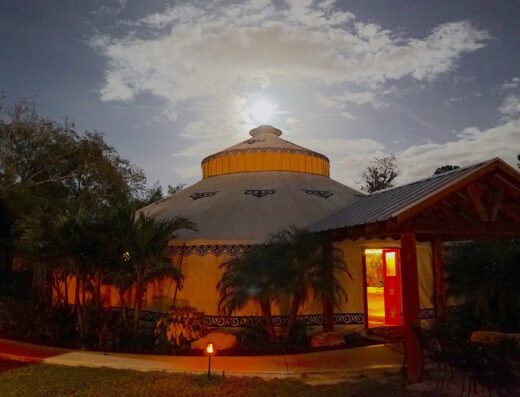 A circular maloka (large hut-style meeting room) is shown glowing in the moonlight