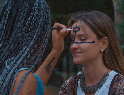 A young woman is having her face painted at an Ayahuasca retreat