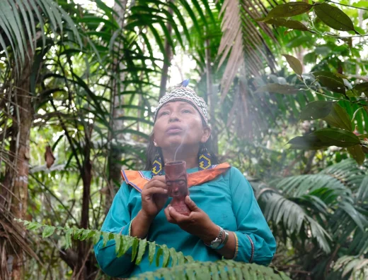 A maestra puffs a ceremonial pipe with the jungle in the background