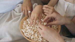 A bowl of popcorn with 5 different hands reaching into it