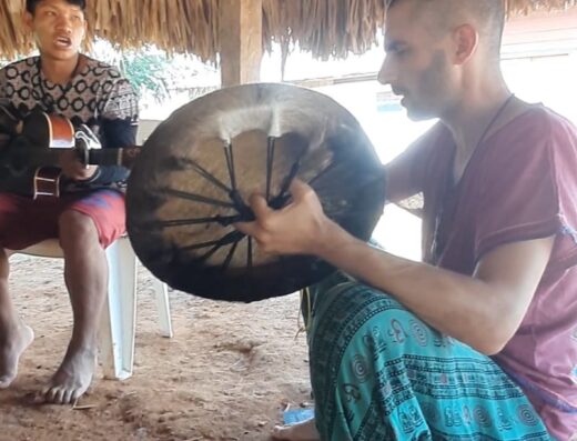 A man is shown beating a animal-skin drum