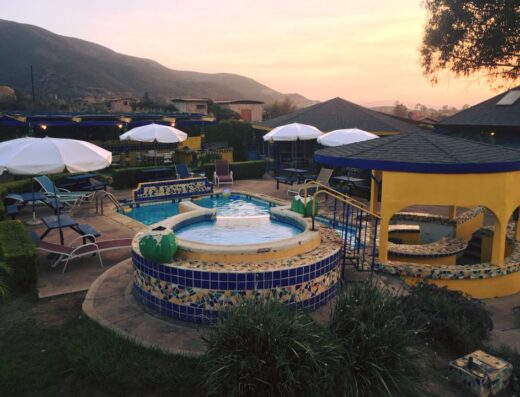 The sun sets behind the mountains in the backdrop of a bubbling hot tub facing the view with white beach umbrellas all around