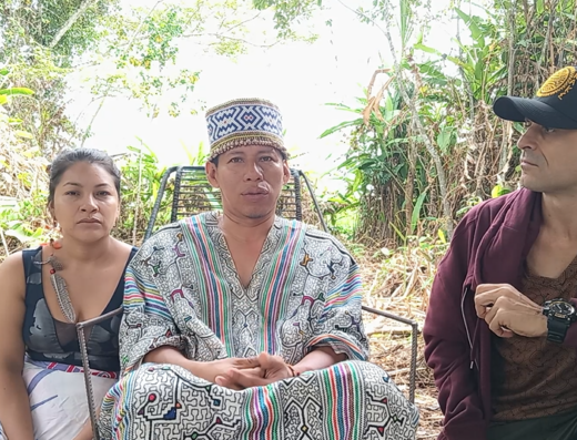 A shaman and his apparent wife or partner sit in front of a jungle