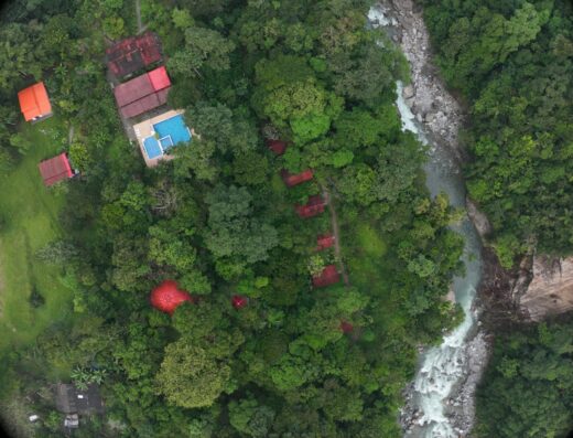 A birds-eye view of a lush, green forest that surrounds several structures with terracotta tile rooves at an Ayahuasca retreat center