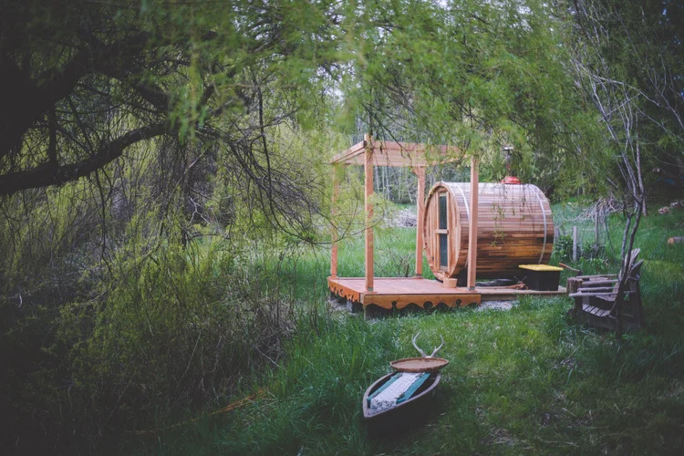A steam barrel sauna sits at the end of a pier that extends over a serene pond